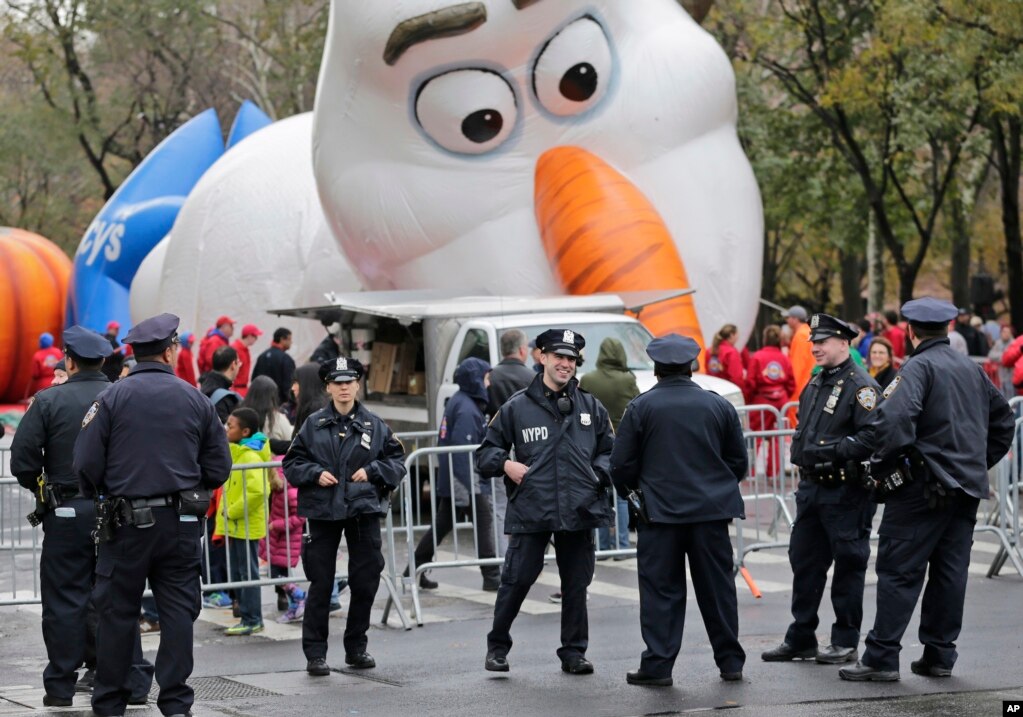 為準備參加紐約感恩節大遊行，“雪寶”氣球正在充氣，警察站在附近（2017年11月22日）。梅西感恩節大遊行中，有流光溢彩的的花車和巨型氣球，也有裝滿沙子的大卡車和警察神槍手來警衛。