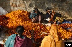 FILE - Indian women and children string garlands of marigolds for sale at a flower market in New Delhi, November 18, 2007.