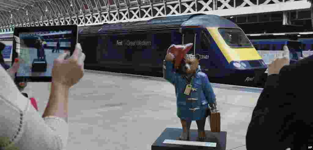 Tourists take photographs on their tablets and smart phone of a statue of &#39;Paddington Bear&#39; on the platform at Paddington railway station in London.