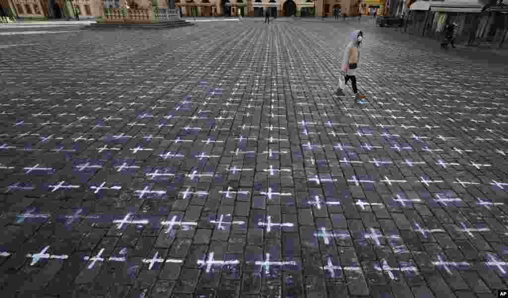 A woman walks at the Old Town Square in Prague, Czech Republic. Thousands of crosses have been painted on a pavement to commemorate the first anniversary since the death of the first COVID-19 patient.