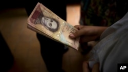 A customer holds a stack of 100-bolivar notes at a bakery in downtown Caracas, Venezuela, Dec. 12, 2016. Venezuelans were rushing to spend their 100-bolivar notes after a surprise announcement that they will be taken out of circulation. More of the new 500-bolivar notes arrived in Venezuela, Dec. 28, 2016. 