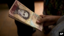 A customer holds a stack of 100-bolivar notes at a bakery in downtown Caracas, Venezuela, Dec. 12, 2016. Venezuelans were rushing to spend their 100-bolivar notes after a surprise announcement that they will be taken out of circulation. More of the new 5