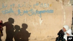 A northern Iraqi woman sits in front of her house with her four children, in the bordertown of Chamchamal, Iraq, March 30, 2003. Writing on wall reads: "This house is for sale."