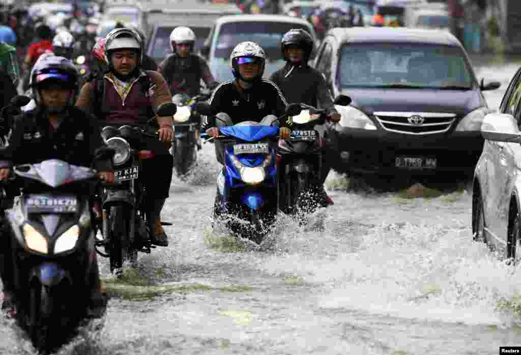 Warga mengendarai sepeda motor mereka melalui jalan yang tergenang banjir di Jakarta. Hujan lebat dalam beberapa hari terakhir telah meningkatkan jumlah wilayah banjir, menyebabkan 64.000 orang harus mengungsi dari rumah mereka.