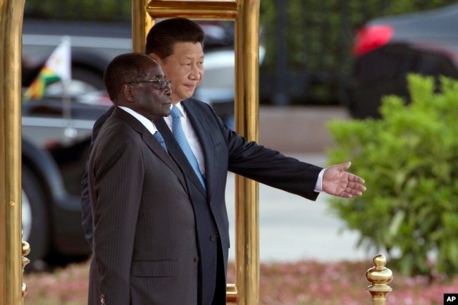 FILE - Chinese President Xi Jinping, right, shows Zimbabwe’s former President Robert Mugabe the way during a welcome ceremony outside the Great Hall of the People in Beijing, China, Aug. 25, 2014.