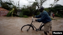 FILE - A man pushes a bicycle through flood waters after Hurricane Matthew passed through Les Cayes, Haiti, Oct. 4, 2016. 
