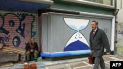 Čistač cipela sedi ispred zatvorene radnje ispisane grafitima u centru Atine, 12. mart, 2012.