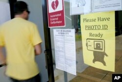 FILE - A voter walks past a "Please Have Photo ID Ready" sign as he enters an early-voting polling place in downtown Little Rock, Ark., May 5, 2014.