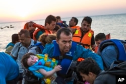 A man carries a girl in his arm as migrants arrive at a coast on a dinghy after crossing from Turkey in the southeastern island of Kos, Greece, during the sunrise early on Aug. 13, 2015.