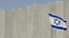 ARCHIVO - Se muestra una bandera israelí plantada frente a la barrera de separación de Israel en la aldea cisjordana de Abu Dis, en las afueras de Jerusalén, el 7 de julio de 2004.