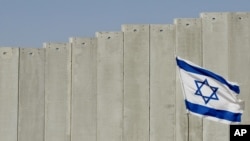 FILE - An Israeli flag is planted in front of Israel's separation barrier in the West Bank village of Abu Dis, on the outskirts of Jerusalem, July 7, 2004. 