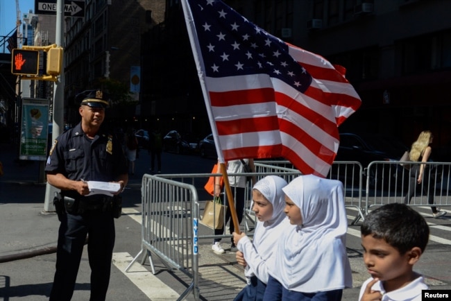 Anak-anak membawa bendera Amerika melewati petugas kepolisian New York dalam pawai tahunan Hari Muslim di New York, 24 September 2017. (Foto: REUTERS/Stephanie Keith)