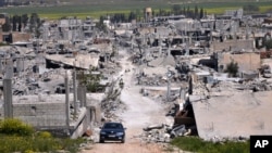 FILE - A car passes in an area that was destroyed during the battle between the U.S.-backed Kurdish forces and the Islamic State fighters, in Kobani, north Syria, April 18, 2015. 