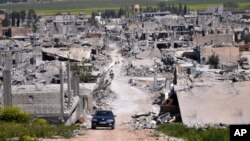 FILE - A car passes in an area that was destroyed during the battle between the U.S.-backed Kurdish forces and the Islamic State fighters, in Kobani, north Syria, April 18, 2015. 