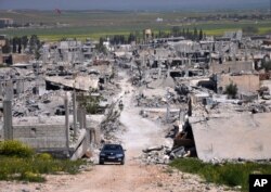 FILE - A car passes in an area that was destroyed during the battle between the U.S.-backed Kurdish forces and the Islamic State fighters, in Kobani, north Syria, April 18, 2015.