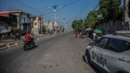 FILE - People ride a motorcycle past a police car following a call for a general strike launched by several professional associations and companies to denounce insecurity in Port-au-Prince on Oct. 18, 2021.