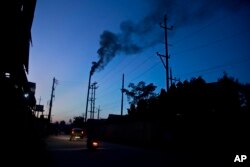 FILE - Traffic moves as smoke emits from the chimney of a factory on the outskirts of Gauhati, India, Oct. 2, 2016.