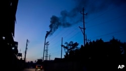 FILE - Traffic moves as smoke emits from the chimney of a factory on the outskirts of Gauhati, India, Sunday, Oct. 2, 2016. 