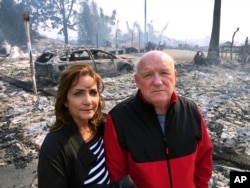 Linda and John Keasler pose for a photo in front of the ruins of their home at the Hawaiian Village Apartments, destroyed when the Thomas fire swept through Ventura, California, Dec. 5, 2017.