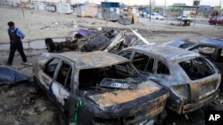 Seorang polisi memeriksa lokasi ledakan bom di lapangan parkir sebuah dealer mobil bekas di Habibiya, Baghdad, Irak (16/4).