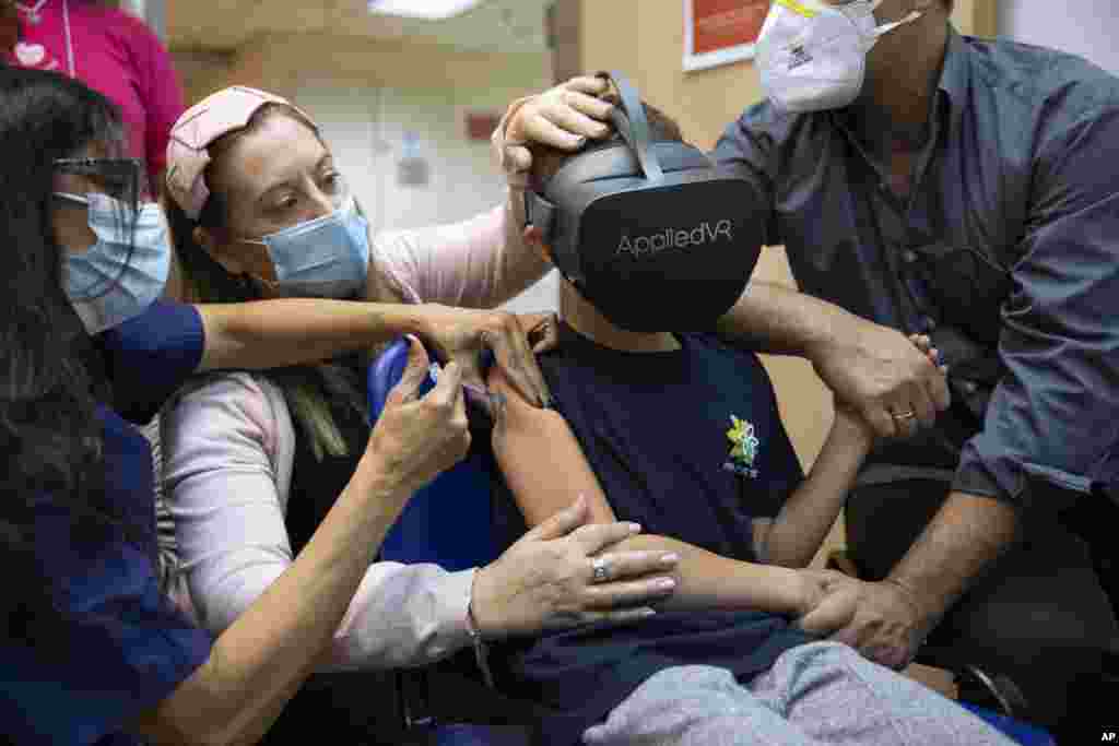 Israeli child Rafael Peled, 8, looks through virtual reality goggles as he receives a Pfizer-BioNTech COVID-19 vaccine from medical workers at the Sheba Tel Hashomer Hospital in Ramat Gan.