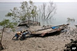 FILE - Villagers help a fisherman couple push their boat to the water at Satyanarayanpur village in the Sundarbans, India. A report says Asia will endure extreme heat, rising sea levels, growing losses from severe weather and increasing food insecurity in coming decades as climate change raises temperatures and alters weather patterns across the globe.