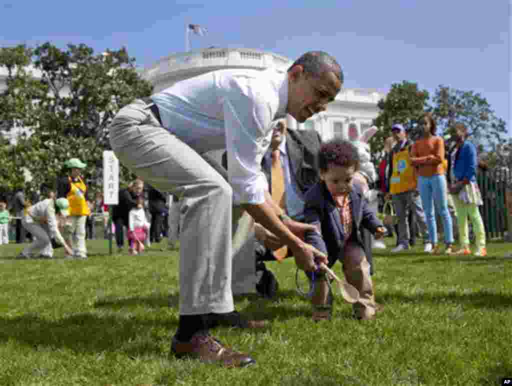 President Barack Obama helps a little boy roll his egg to the finish line during the annual White House Easter Egg Roll, Monday, April 9, 2012, on the South Lawn of the White House in Washington. In the background, at left are Malia Obama and Sasha Obama