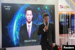 FILE - Xinhua news anchor Qiu Hao stands next to an AI virtual news anchor based on him, at a Sogou booth during an expo at the fifth World Internet Conference in Wuzhen town of Jiaxing, Zhejiang province, China, Nov. 7, 2018.