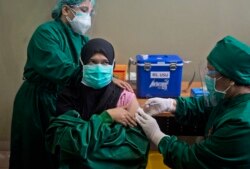 FILE - In this Wednesday, Jan. 20, 2021 file photo, Dr. Lili Rahmawaty, right, gives a shot of COVID-19 vaccine to a colleague at North Sumatra University Hospital in Medan, North Sumatra, Indonesia. (AP Photo/Binsar Bakkara)
