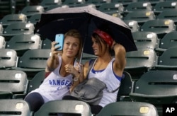 These two baseball fans take selfies under an umbrella during a rain delay of a game between the Texas Rangers and Seattle Mariners Sept. 2014, in Texas. (AP Photo/LM Otero)