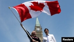 Une sportive canadienne tient le drapeau national près du Premier ministre Justin Trudeau au Parliament Hill à Ottawa, Ontario, Canada, le 21 juillet 2016. 