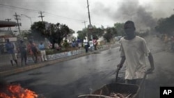 A man pushes a wheelbarrow past a barricade of burning tires in Port-au-Prince, Haiti, Thursday Dec. 9, 2010