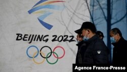 FILE - People walk past the Beijing 2022 Winter Olympics logo, at Shougang Park in Beijing, China, Dec. 1, 2021. 