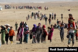 FILE - Displaced people from the minority Yazidi sect, fleeing violence from forces loyal to the Islamic State in Sinjar town, walk towards the Syrian border, on the outskirts of Sinjar mountain, near the Syrian border town of Elierbeh of Al-Hasakah Governorate, Aug. 11, 2014.