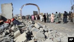 File - Afghan security forces and civilians walk at the site of a suicide attack in Lashkar Gah, capital of Helmand province, Afghanistan, June 2015. 