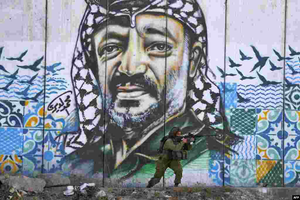 A member of the Israeli border guards looks through the scope of an assault rifle as he stands by a mural showing a graffiti image of late Palestinian leader Yasser Arafat, at the Qalandiya checkpoint near the West Bank city of Ramallah.