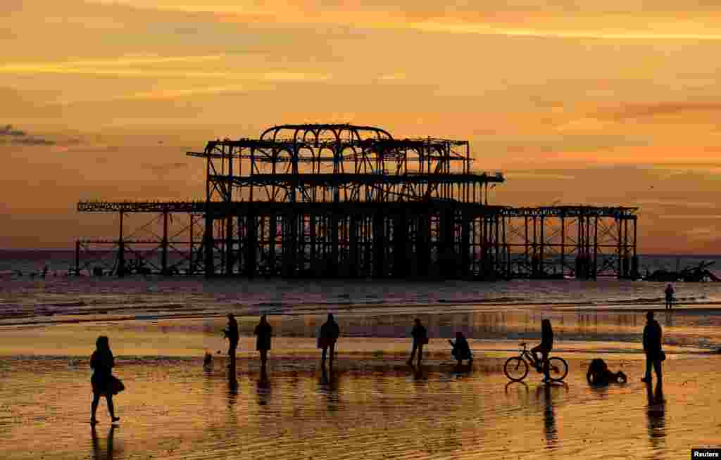 Beachgoers view the sunset with the remains of the West Pier seen on the coastline at Brighton in southern England.