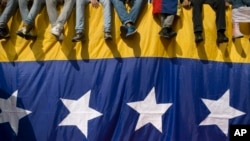 En esta foto la gente se sienta en una pared cubierta por una bandera venezolana durante una protesta contra el presidente Nicolás Maduro en Caracas, Venezuela.