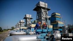 FILE - Workers stand near pipes at a gas compressor station near Uzhhorod May 21, 2014. 