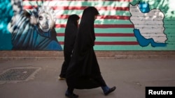 FILE - Iranian women walk past an anti-U.S. mural on the wall of the former U.S. embassy in Tehran, Oct. 12, 2011. 