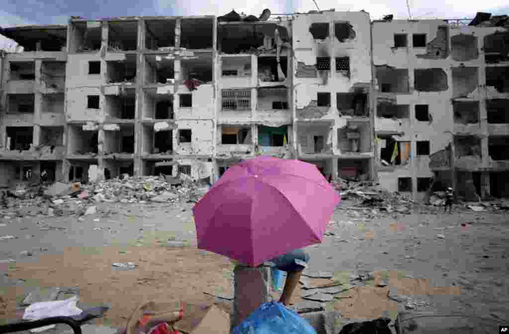 A Palestinian boy holds an umbrella as he rests in front of the damaged Nada Towers residential neighborhood in the town of Beit Lahiya, northern Gaza Strip, Aug. 11, 2014.