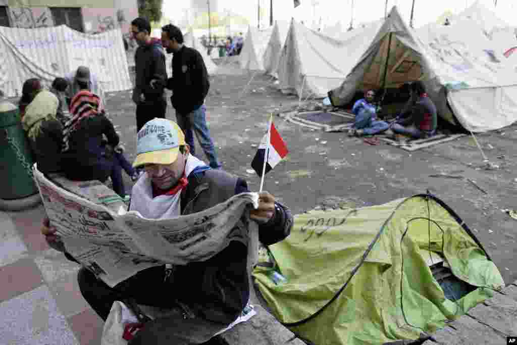 An Egyptian protester reads the newspaper as others sit next to their tents in Tahrir Square in Cairo, December 9, 2012