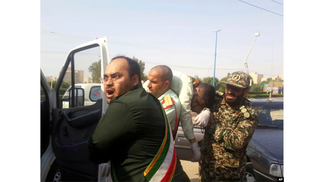 In this photo provided by the Iranian Students' News Agency, ISNA, Revolutionary Guard members carry a wounded comrade after a shooting during their parade marking the 38th anniversary of Iraq's 1980 invasion of Iran, in the southwestern city of Ahvaz, Iran, Sept. 22, 2018.