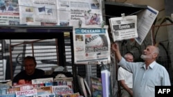 FILE - A man reads newspapers' headlines in central Athens, Aug. 21, 2018, as the country ended eight years of painful bailouts. On Monday, eurozone ministers delayed granting Greece debt relief because the government failed to implement reforms promised during the bailout.