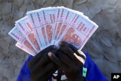 FILE - A man holds a handful of 5 Billion Zimbabwean dollar notes, in Harare, Friday, June, 12, 2015.