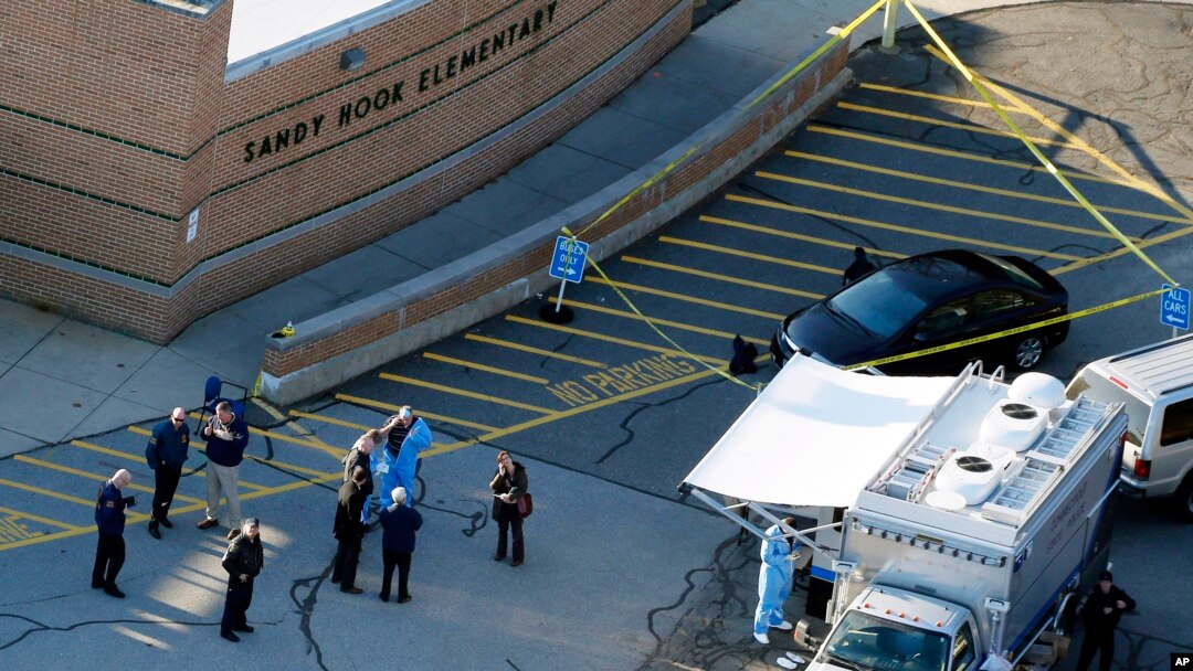 FILE - Officials stand outside of Sandy Hook Elementary School in Newtown, Conn., where authorities gunman Adam Lanza opened fire inside the school killing 20 first-graders and six educators at the school and killed himself as police arrived.