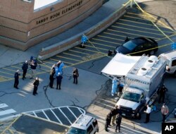 FILE - Officials stand outside of Sandy Hook Elementary School in Newtown, Conn., where authorities gunman Adam Lanza opened fire inside the school killing 20 first-graders and six educators at the school, and killed himself as police arrived, Dec. 14, 20