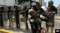 Una mujer suena una cacerola al pasar frente a guardias nacionales bolivarianos en Caracas.