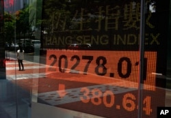 A woman walks past a bank electronic board showing the Hong Kong share index outside a Hong Kong local bank, July 3, 2013.
