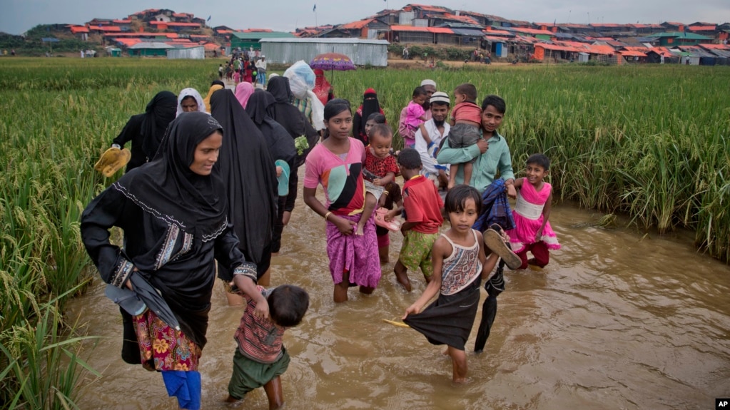 FILE - Rohingya Muslims, who crossed over from Myanmar into Bangladesh, wade past a waterlogged path leading to the Jamtoli refugee camp in Ukhiya, Bangladesh, Nov. 17, 2017.